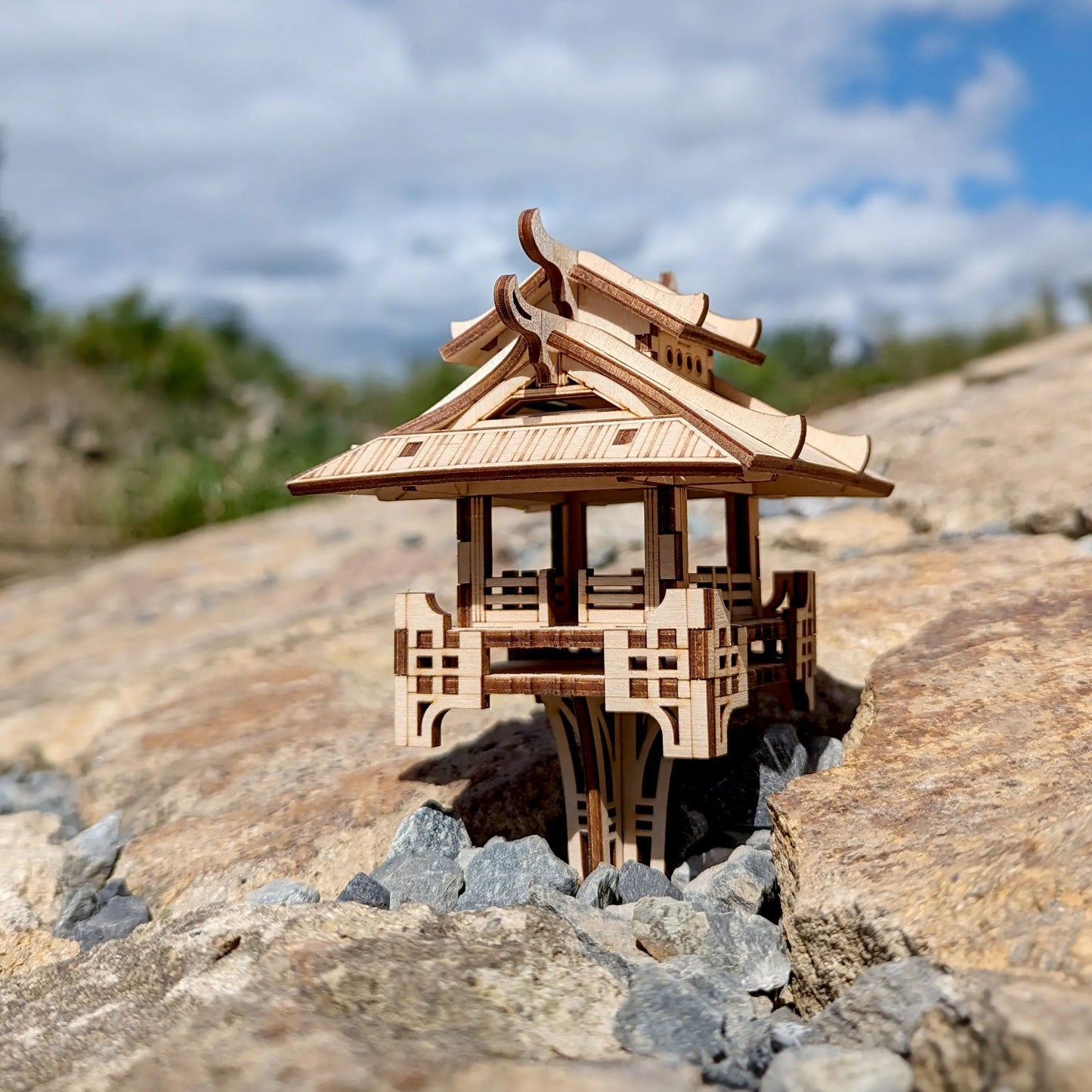 Profile perspective of an oriental miniature gazebo made of laser cut plywood, beautifully staged on weathered rocks.