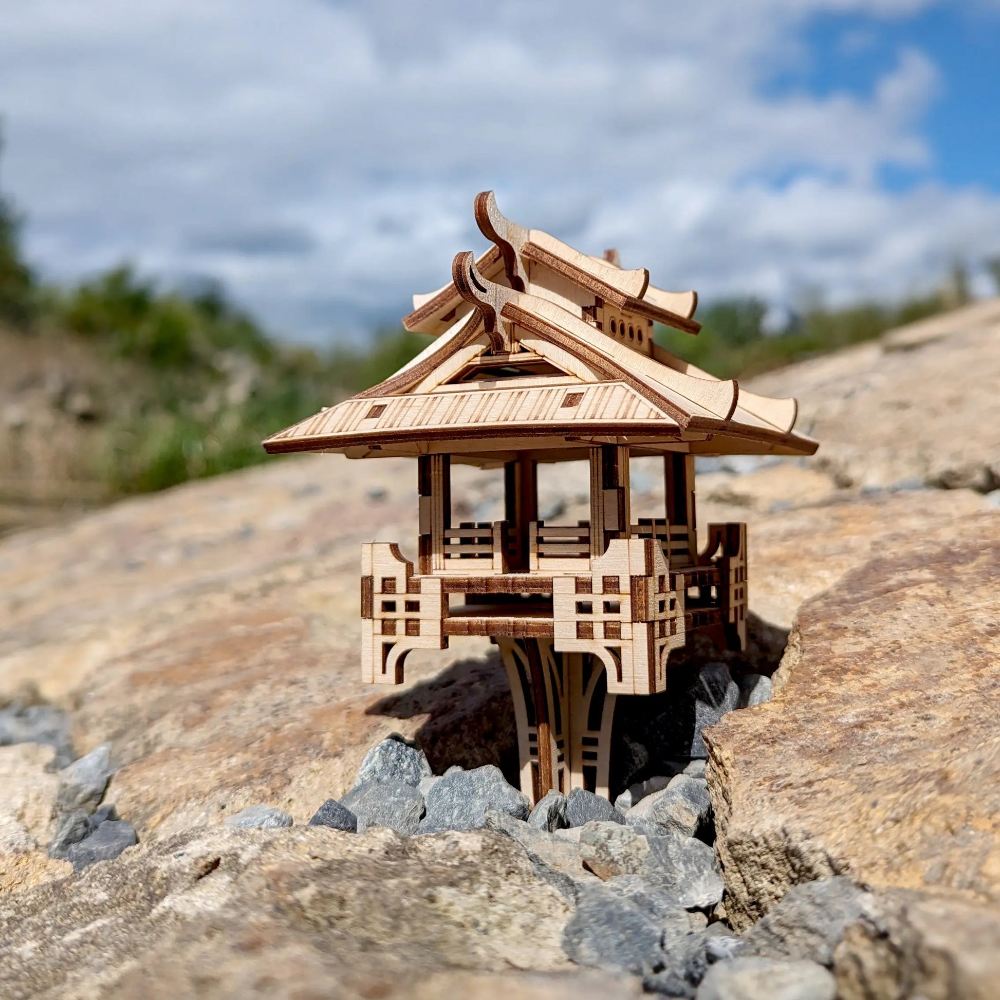 Profile perspective of an oriental miniature gazebo made of laser cut plywood, beautifully staged on weathered rocks.