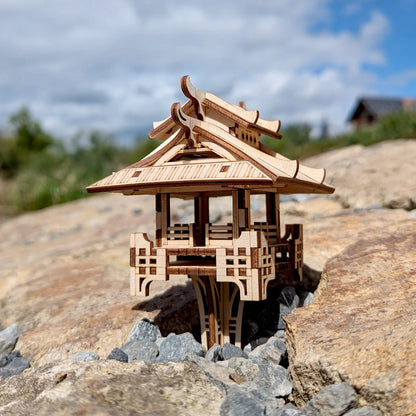 Low-angle side shot of a laser cut plywood oriental temple miniature standing on rocky ground under a bright blue sky.