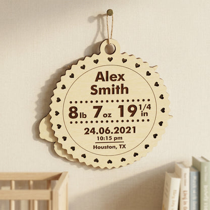 The back of a personalized laser-cut wooden baby plaque, showcasing engraved birth statistics. Includes the name "Alex Smith," weight, length, date, time, and city (Houston, TX). The light wood ornament features a decorative heart-scalloped edge and hangs in a modern nursery setting.