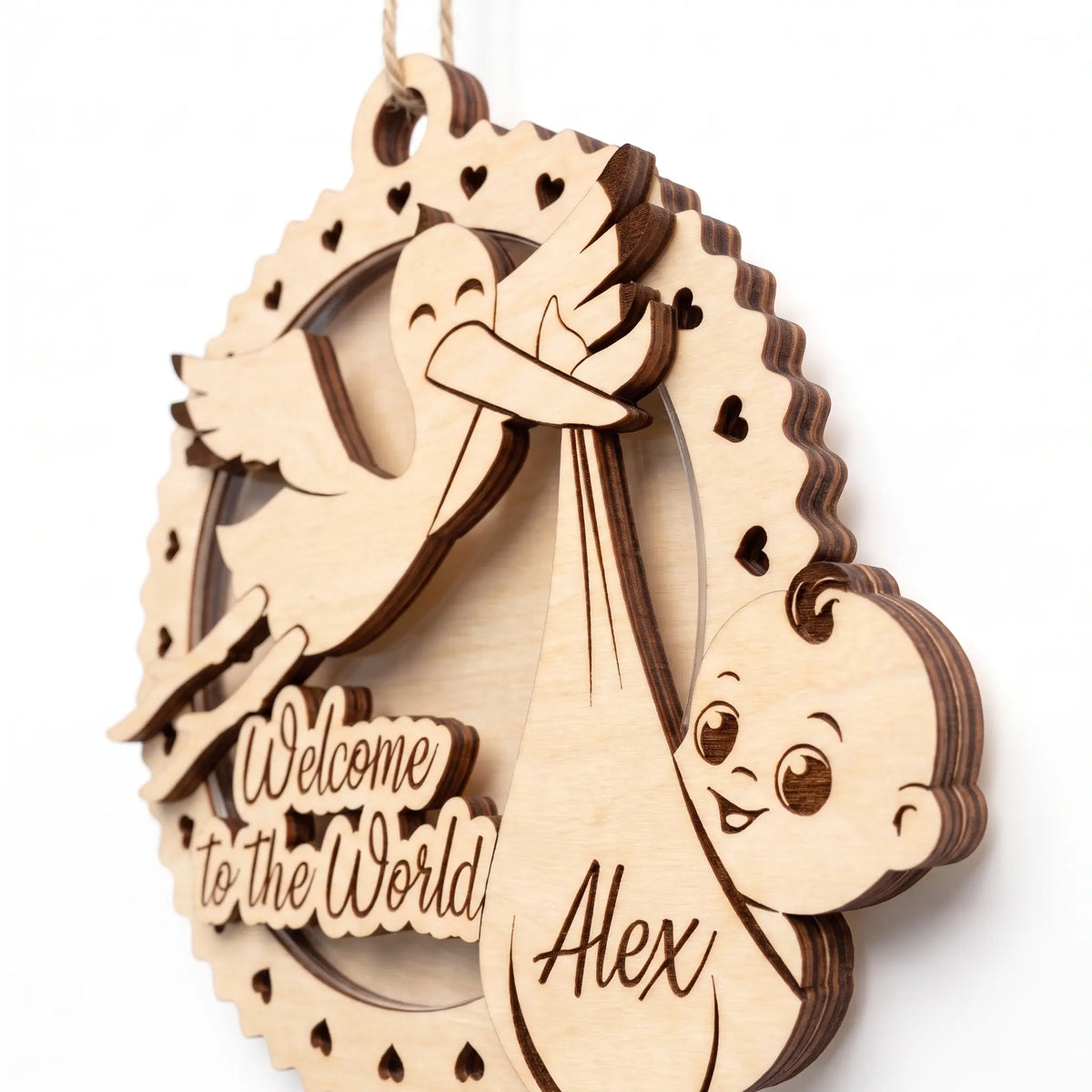 Close-up of laser cut plywood baby birth ornament showing flying stork holding newborn swaddle bundle and heart frame edge.