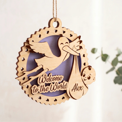 Laser cut plywood newborn baby birth ornament hanging by twine string next to green eucalyptus leaves on light background.