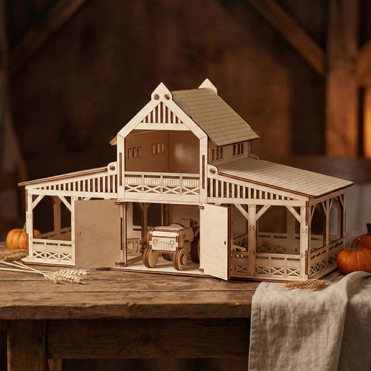 Laser cut plywood toy barn with open stable doors on a wooden table. A small wooden tractor sits inside the central bay. The structure features intricate railings, a peaked roof, and a decorative balcony.