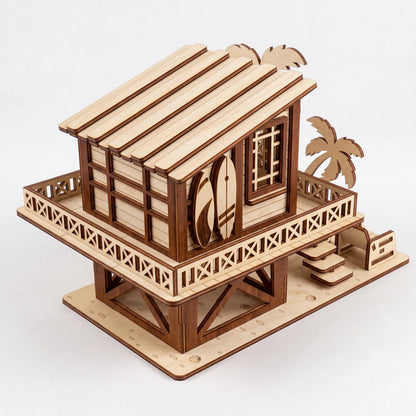 Three-quarter view of a laser-cut birch plywood beach house model featuring a wraparound balcony, surfboards, and palm trees.