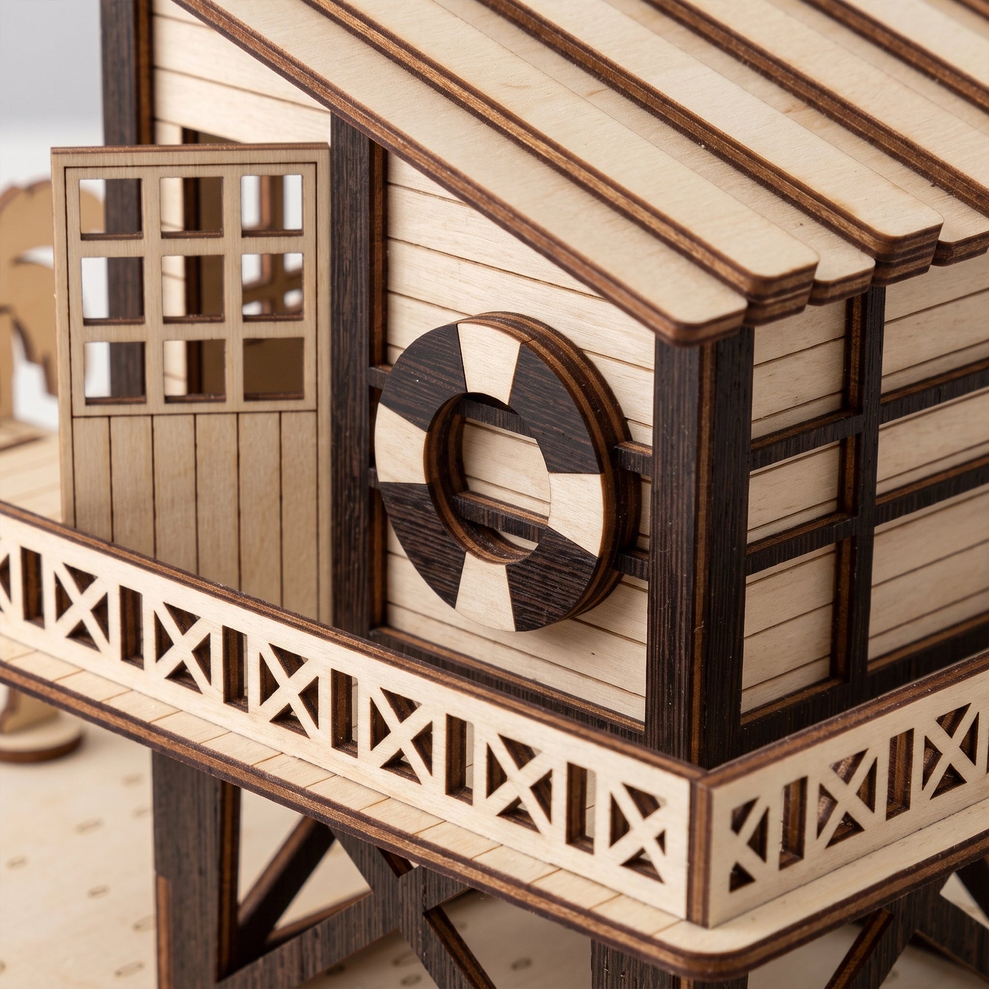 Close-up of a laser-cut birch plywood beach house balcony with a life ring, open door, and realistic dark burnt edges.