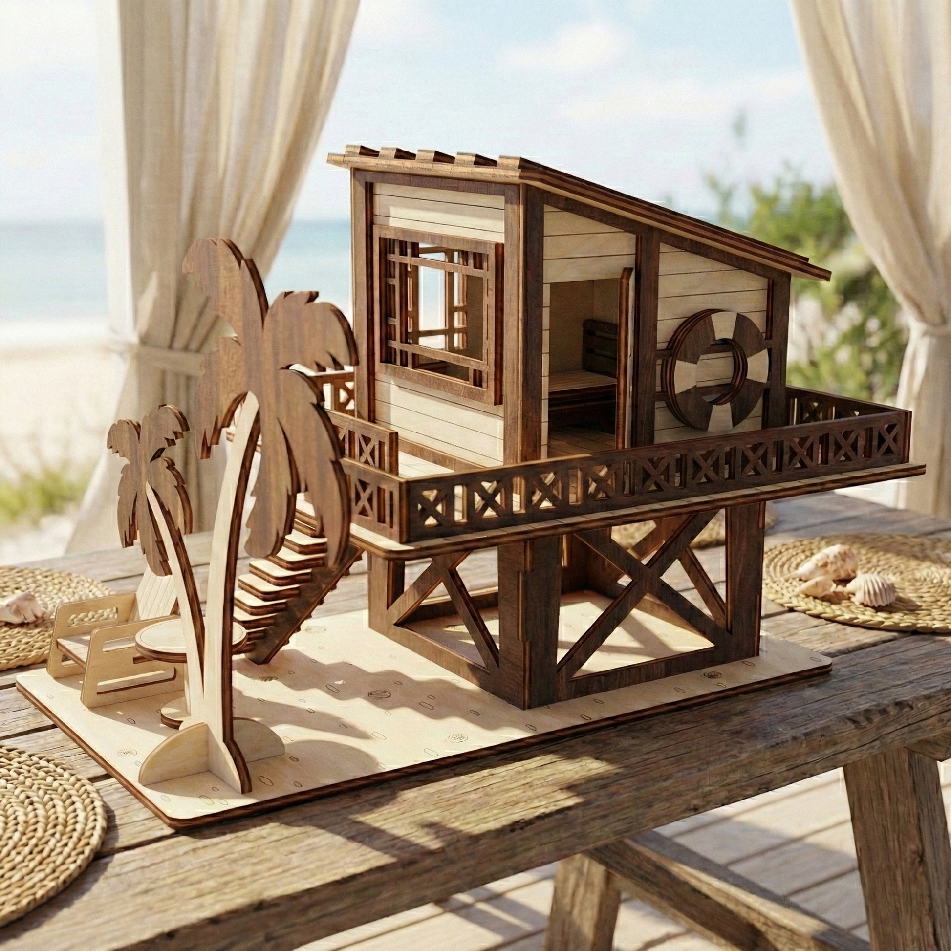 A laser cut plywood beach house model on a rustic deck. It features a stilt base, balcony, palm trees, and lounge chair. In the background, a sunny beach is visible through white curtains.