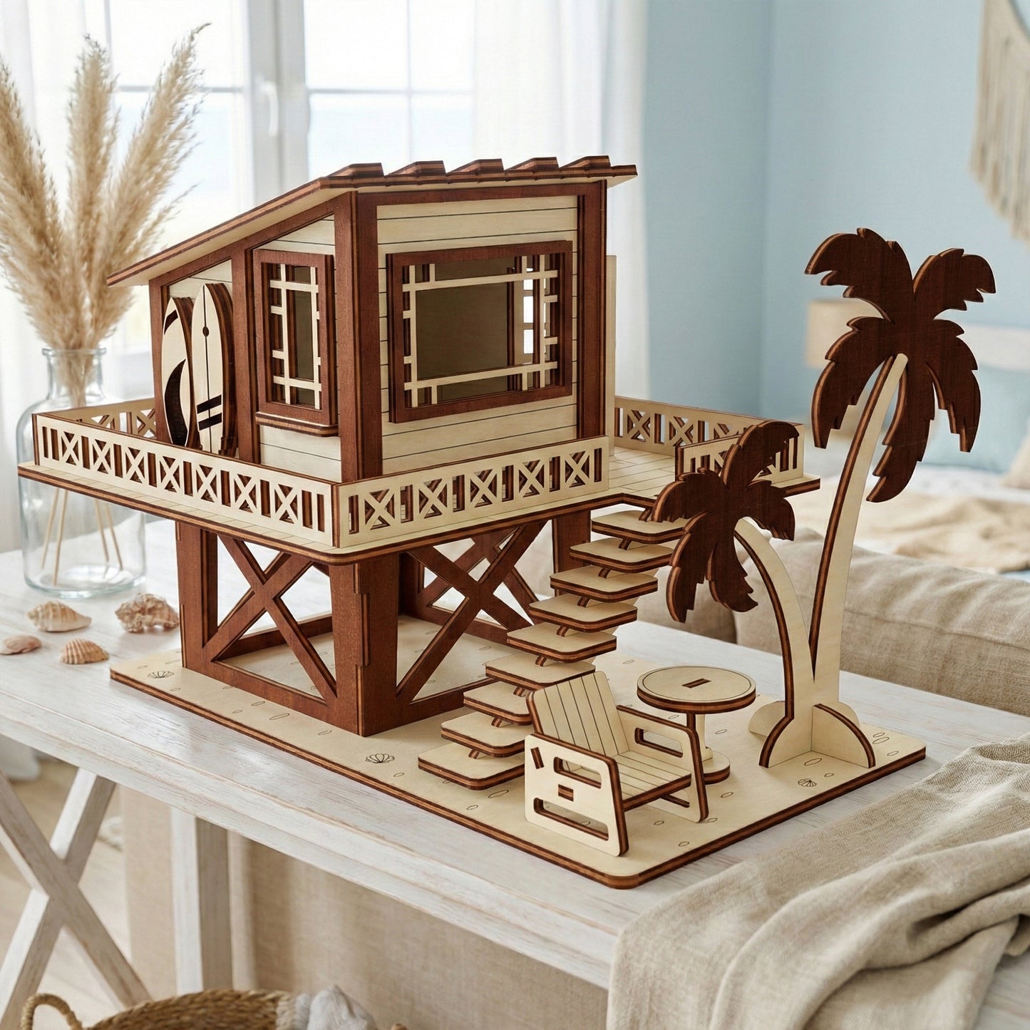 Front view of a 3D laser cut plywood surf shack on a white table. Detailed with surfboards, a staircase, and a palm tree. The light wood contrasts with dark burnt edges in a bright, modern interior.