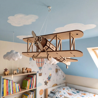 A wooden laser cut toy airplane suspended from the ceiling in a child's bedroom, with a bookshelf filled with books and toys in the background.
