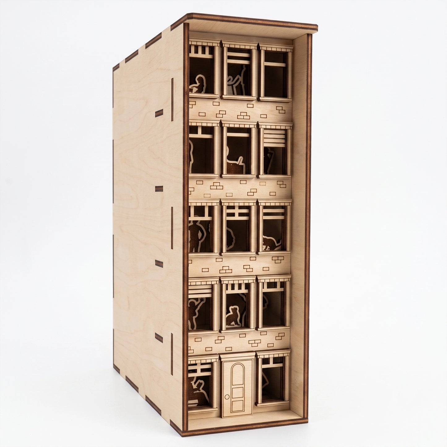 Front view of a laser-cut birch plywood apartment house book nook showing multi-story windows, silhouettes, and dark burnt edges.