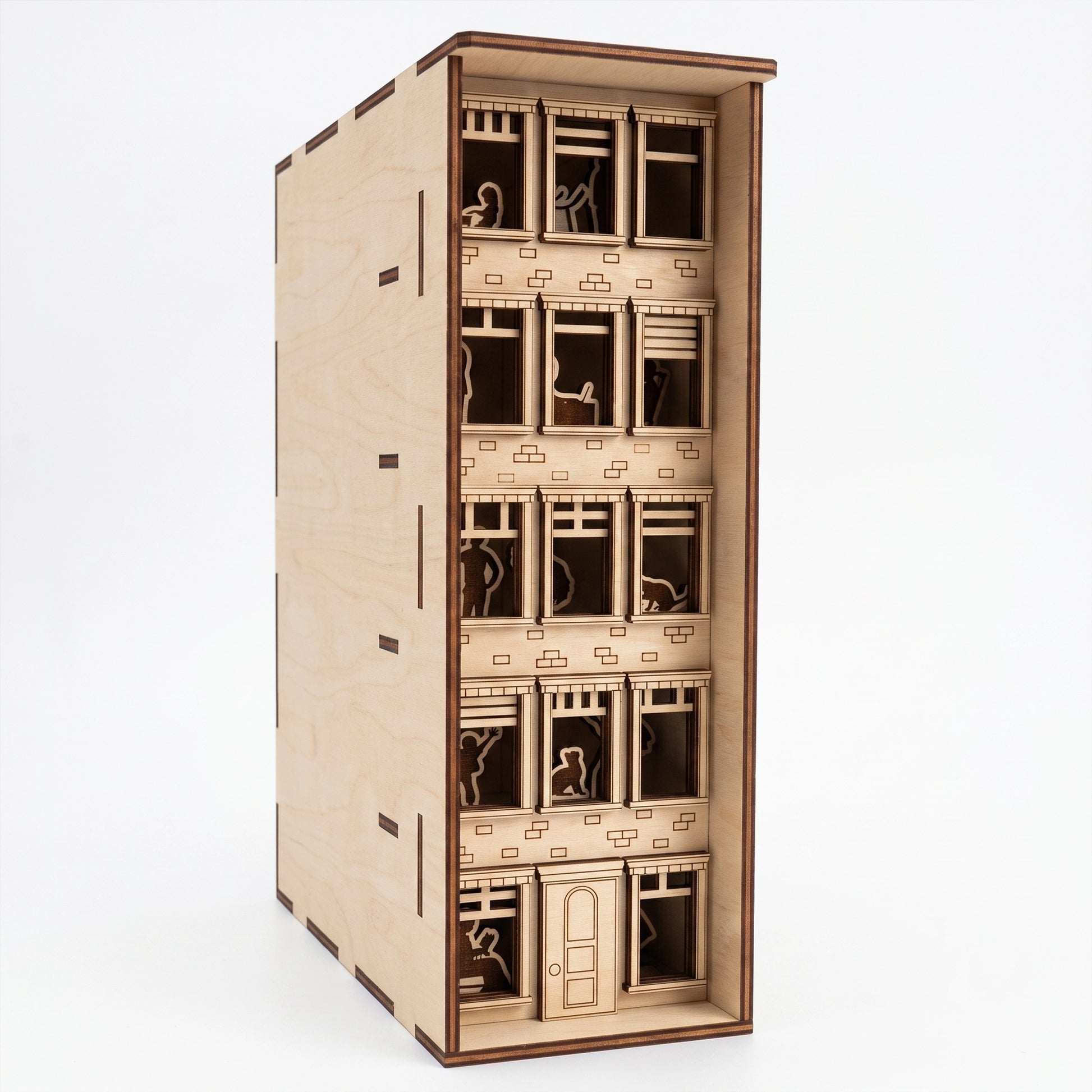 Front view of a laser-cut birch plywood apartment house book nook showing multi-story windows, silhouettes, and dark burnt edges.