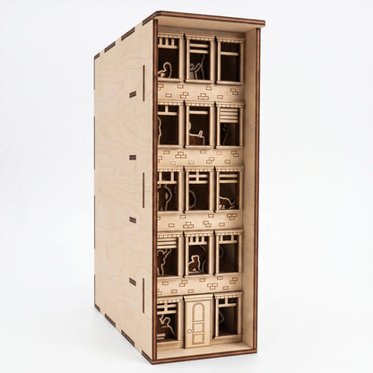 Front view of a laser-cut birch plywood apartment house book nook showing multi-story windows, silhouettes, and dark burnt edges.