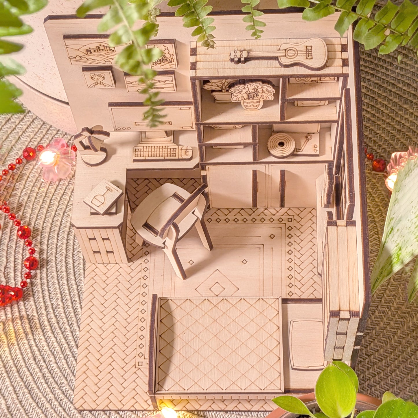 Wooden model of a room with furniture on a textured surface with plants around