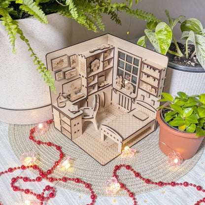 Miniature laser cut wooden book nook model of a house with furniture and decorations, surrounded by potted plants and string lights.