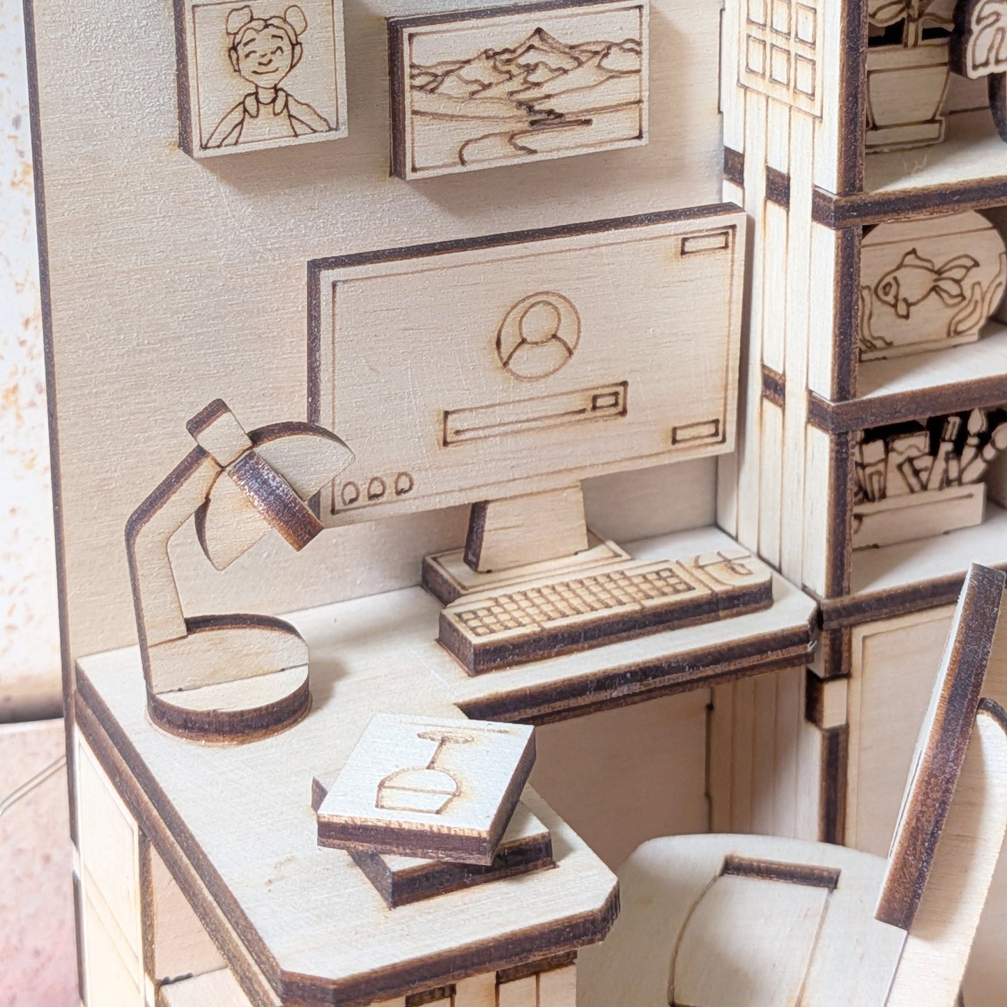 Close-up of a miniature wooden desk and chair in a dollhouse bedroom book nook, showing laser cut details of a computer, lamp, books and shelves. Digital laser cutting file for SVG DXF AI CDR