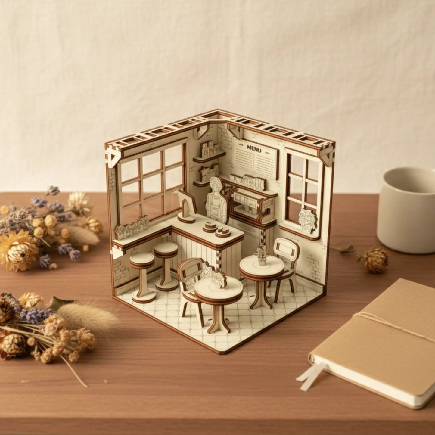 Miniature laser cut plywood cafe kit on a desk, styled with dried lavender bouquets and a blank notebook nearby.