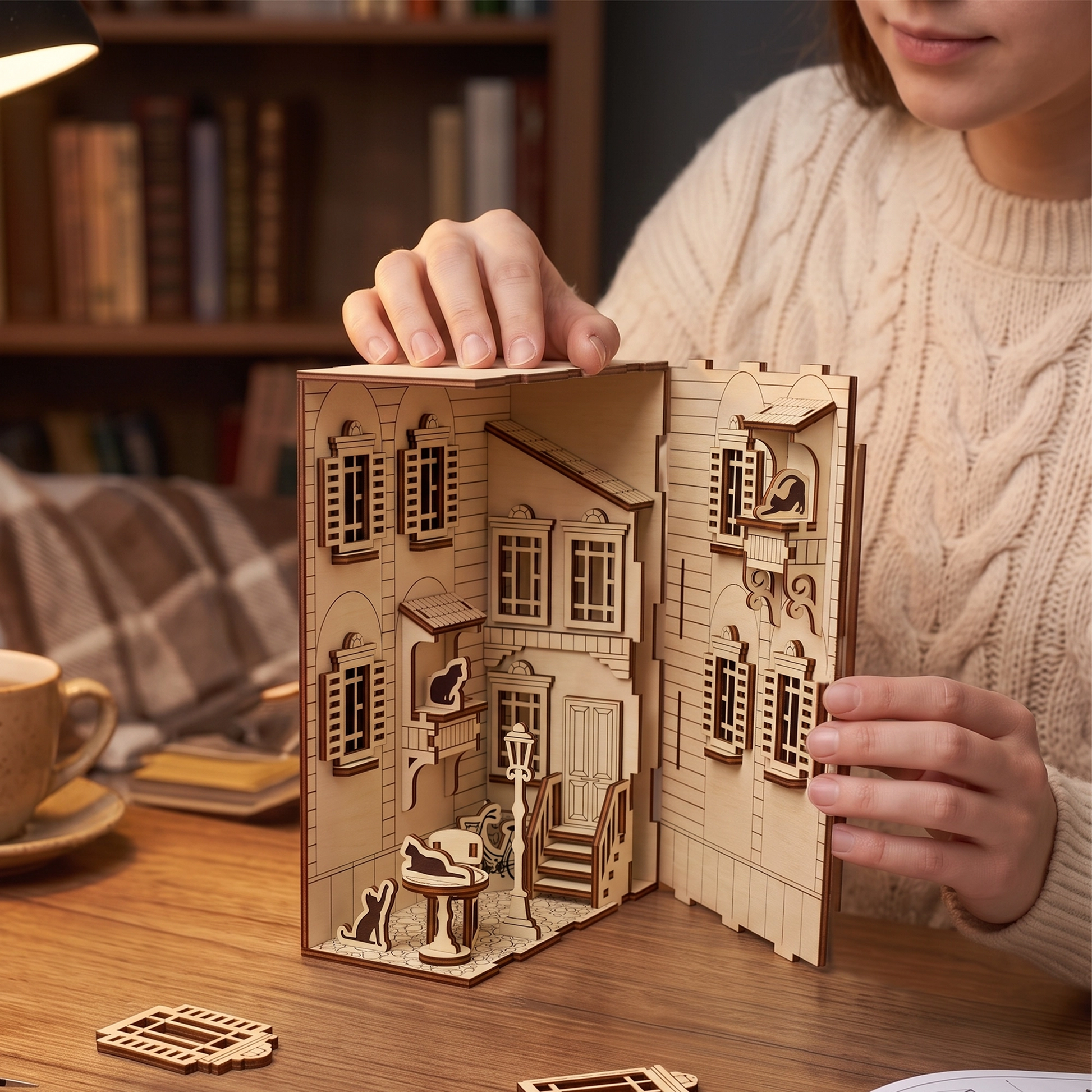 A person assembling a French yard book nook model, demonstrating the detailed laser cut plywood components.