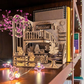 Wooden laser cut Book nook greenhouse dollhouse model with intricate details on a decorative surface with plants.