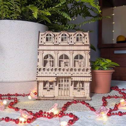 Laser cut townhouse book nook displayed on a white mat with plants and string lights, showing multiple floors and figures inside.