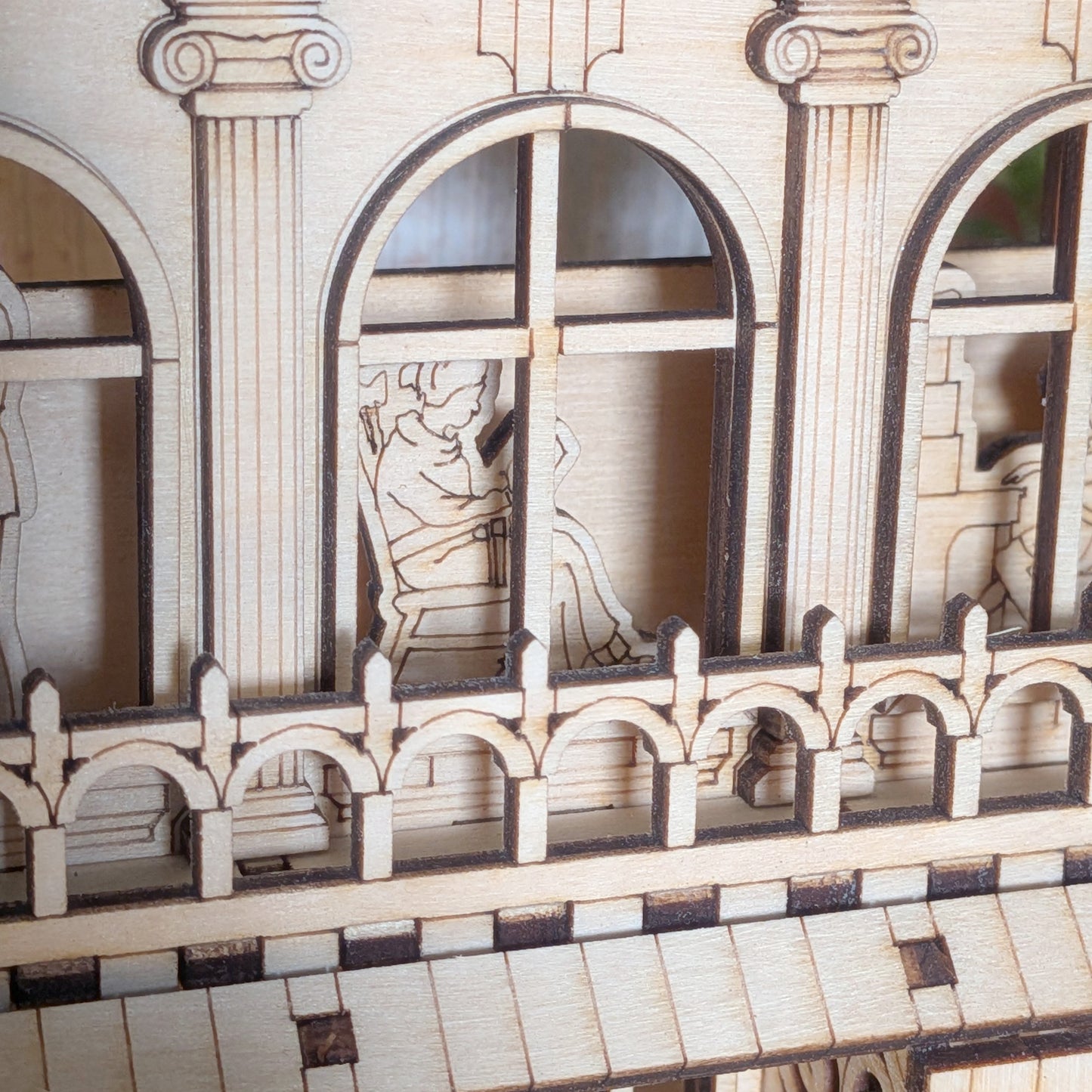 Close-up of a laser cut figure sitting inside the book nook, visible through an arched window and framed by decorative balcony railings