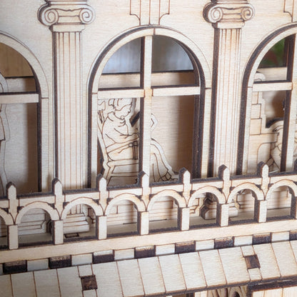 Close-up of a laser cut figure sitting inside the book nook, visible through an arched window and framed by decorative balcony railings