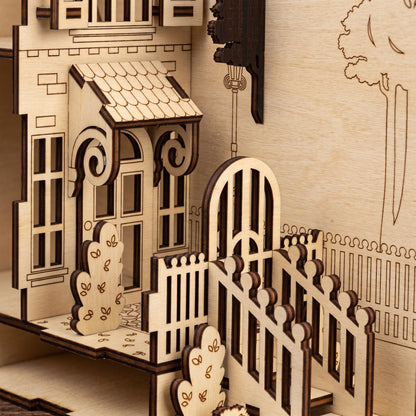 Close-up of a laser-cut birch plywood romantic house book nook front porch, stairs, fence, and dark burnt edges.