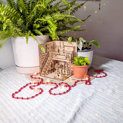 Laser-cut wooden music store book nook displayed on a table surrounded by plants and decorative LED lights