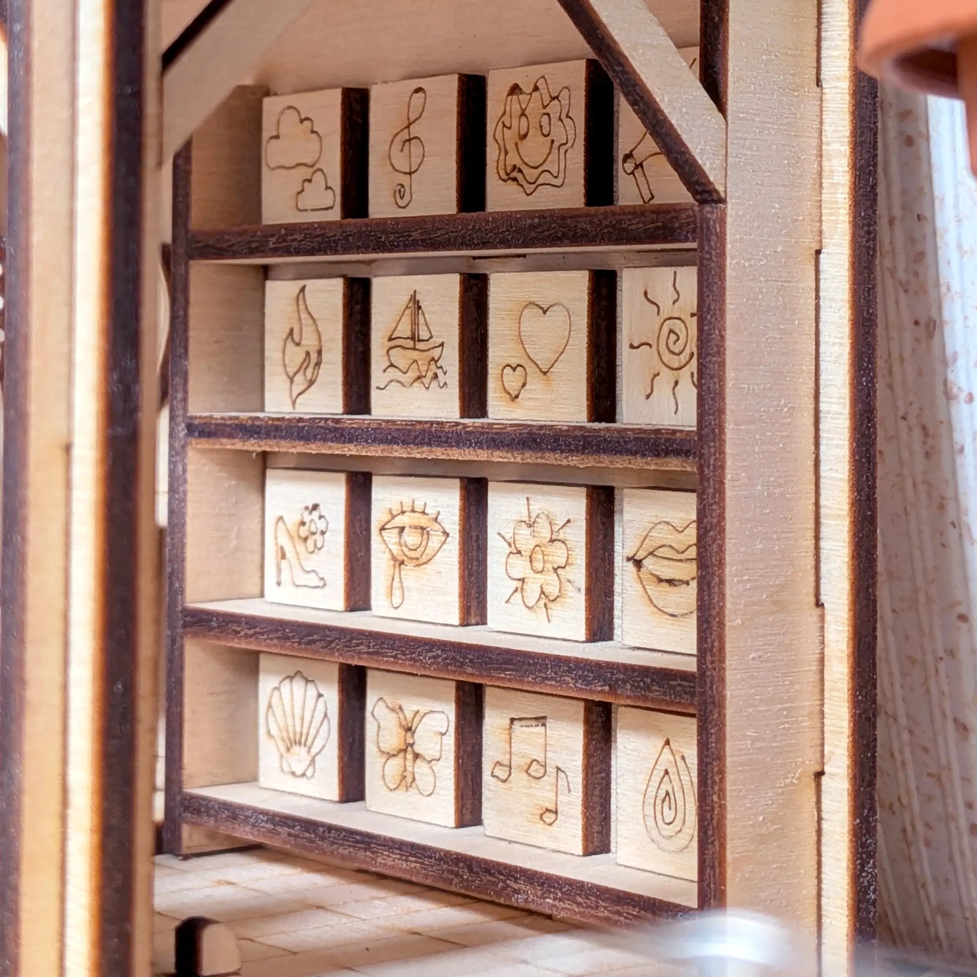 Close-up of a tiny display shelf with engraved decorative icons inside a music nook made of laser cut plywood.
