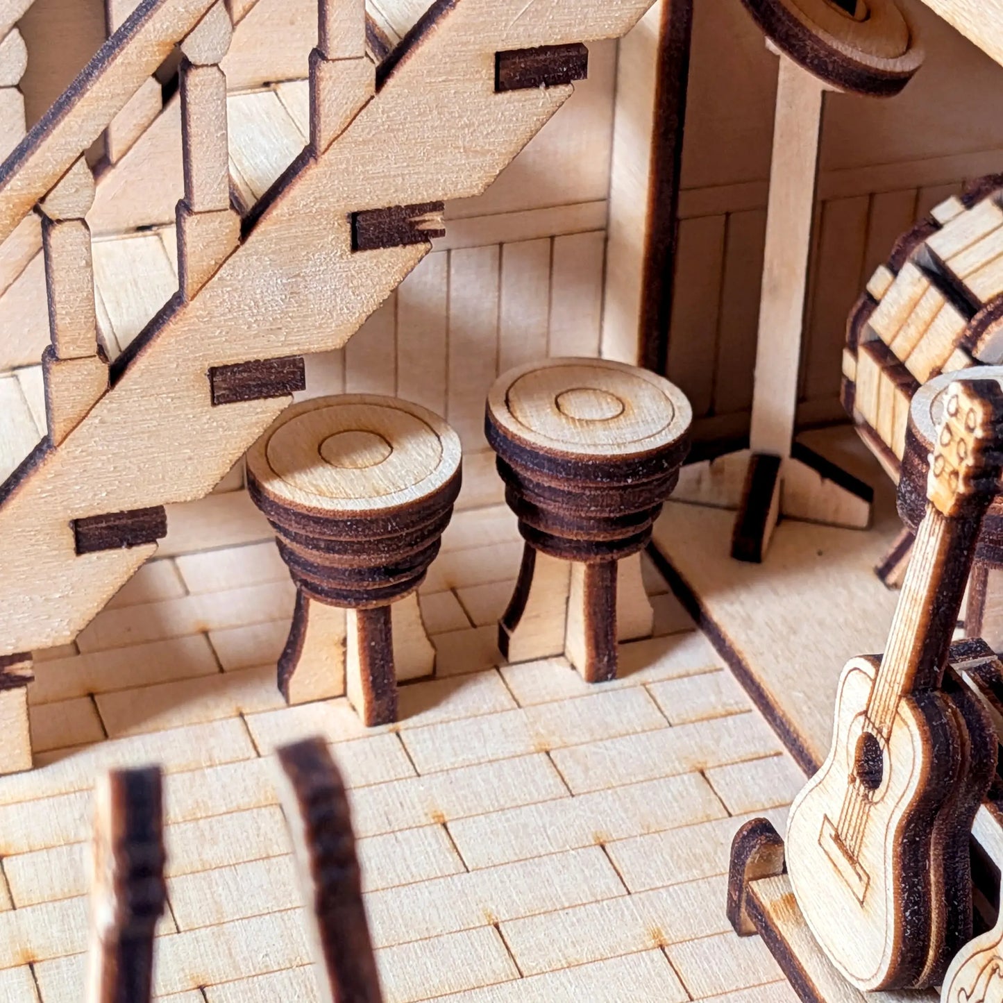 Macro shot of miniature bar stools and a tiny guitar under the stairs inside a laser cut plywood music roombox kit.