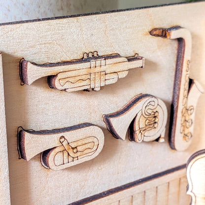 Close-up of laser-cut wooden brass instruments including trumpet, tuba, horn and saxophone mounted on the book nook wall