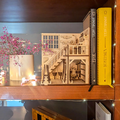 Laser cut plywood music store book nook tucked on a bookshelf next to hardback novels and a vase of pink blossoms.