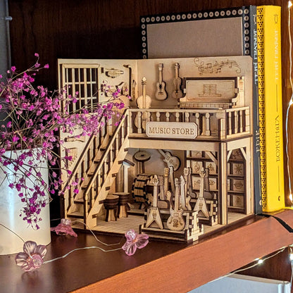 Laser cut plywood music store book nook on a dark wood shelf next to violet flowers and colorful book spines.