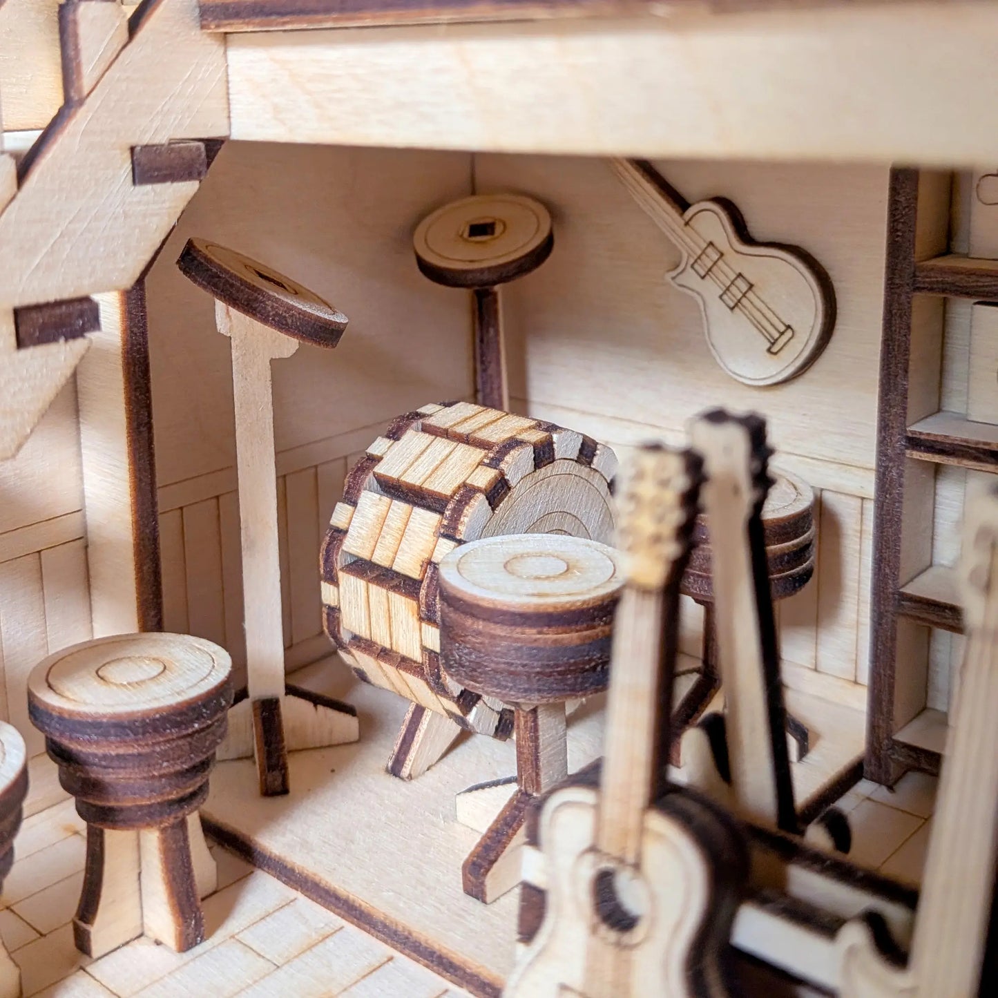 Tiny drum set and cymbals arranged in the back room of a miniature music store crafted from laser cut plywood layers.