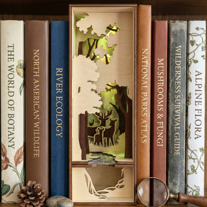A laser cut wooden Book Nook Nature diorama featuring a multi-layered forest scene with deer silhouettes, placed against a wooden library shelf background.
