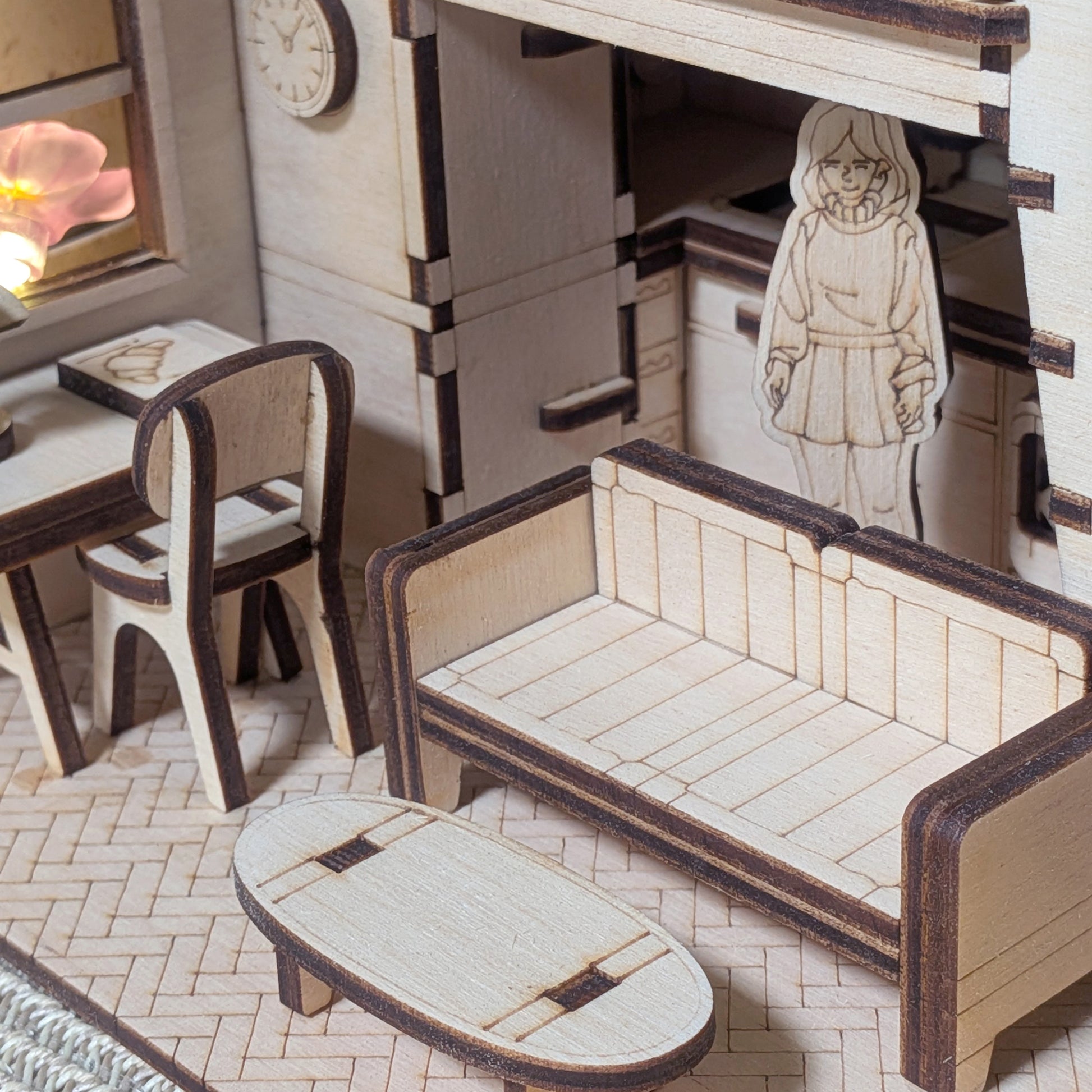 Miniature wooden living room scene with a sofa, small table, desk and a standing character figure. Part of a dollhouse book nook made from a laser cut wooden diorama template