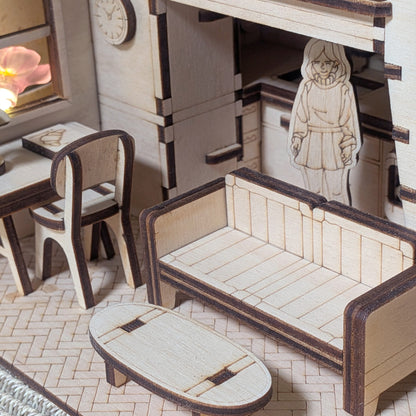 Miniature wooden living room scene with a sofa, small table, desk and a standing character figure. Part of a dollhouse book nook made from a laser cut wooden diorama template