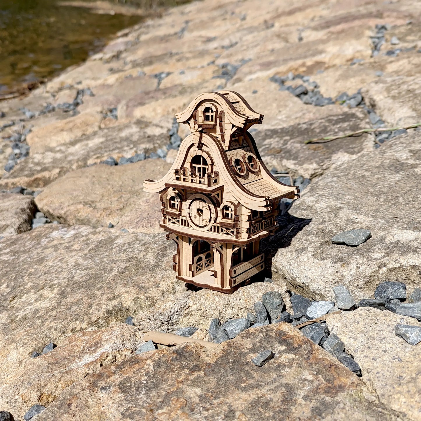 Whimsical laser cut plywood bunny house model with small carrot details resting on a vibrant green mossy rock in the woods.