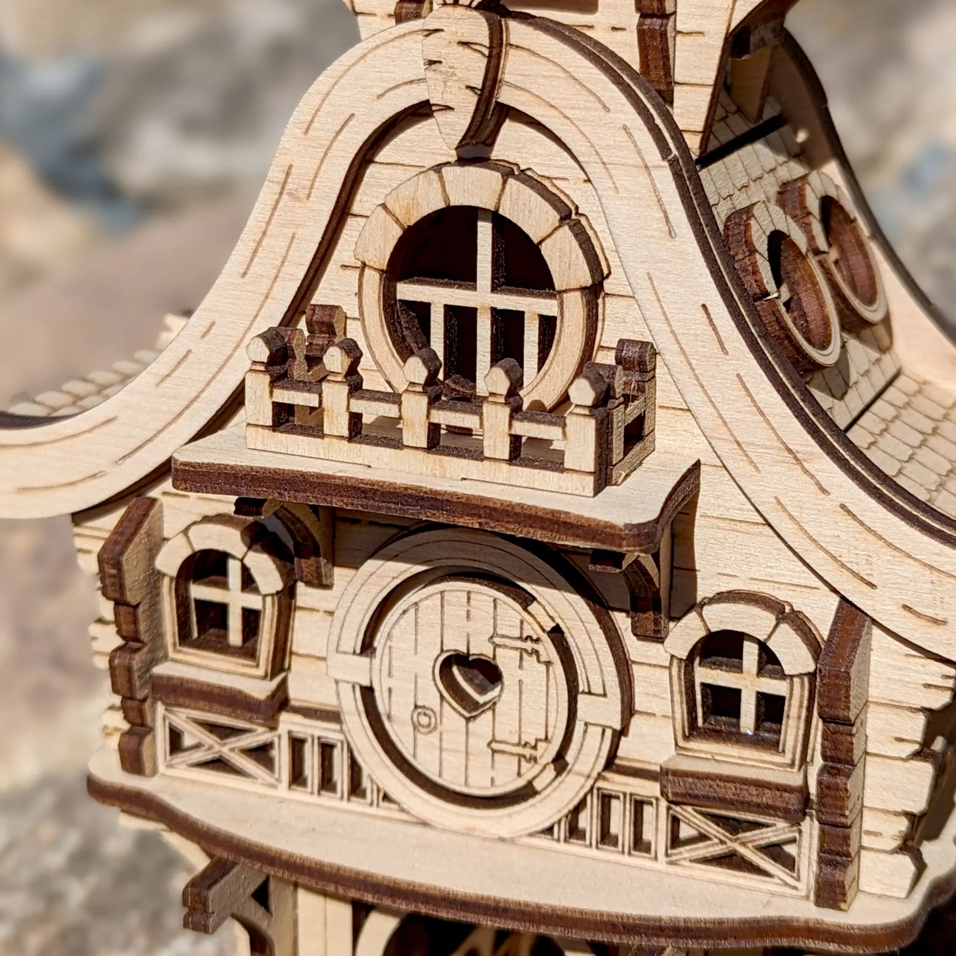 Easter themed laser cut plywood bunny house model with a tiny fence placed on a grey garden stone in warm spring sunlight.