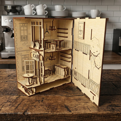 An opened laser cut wooden Café Book Nook revealing a two-story miniature interior with tables, a counter, and tiny decor, placed on a wooden surface with a kitchen background.