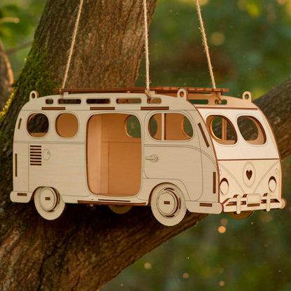 Laser cut wooden  plywood Camper Van Birdhouse or treat dispenser, hanging by twine ropes from a mossy tree branch. The detailed design, resembling a vintage bus with windows and a roof rack, is illuminated by warm golden-hour light against a blurred green forest backdrop. Perfect DIY craft kit for garden decor and bird feeding.