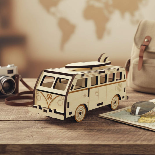 Laser cut wooden plywood camper van miniature with a surfboard on top. Vintage style plywood model with engraved logo, resting on a wooden table next to a camera, map, and backpack. Detailed 3D wood puzzle for travel lovers.