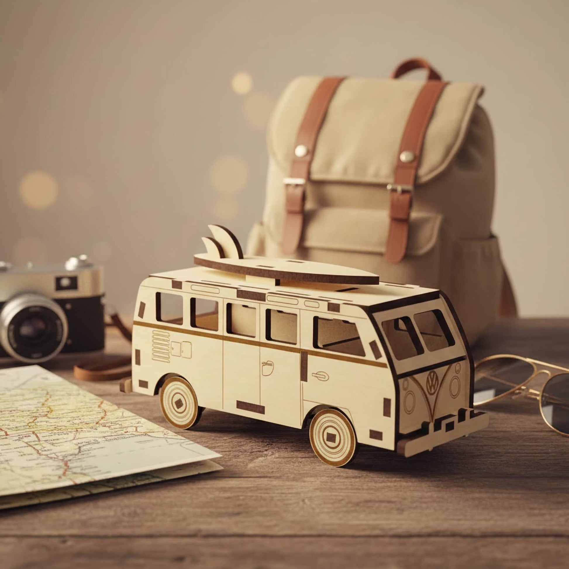 Side profile of a laser cut wooden plywood surfboard camper van. Shows intricate window cutouts and engraved door details. Displayed in a cozy travel-themed setting with a backpack, sunglasses, and map in the background.