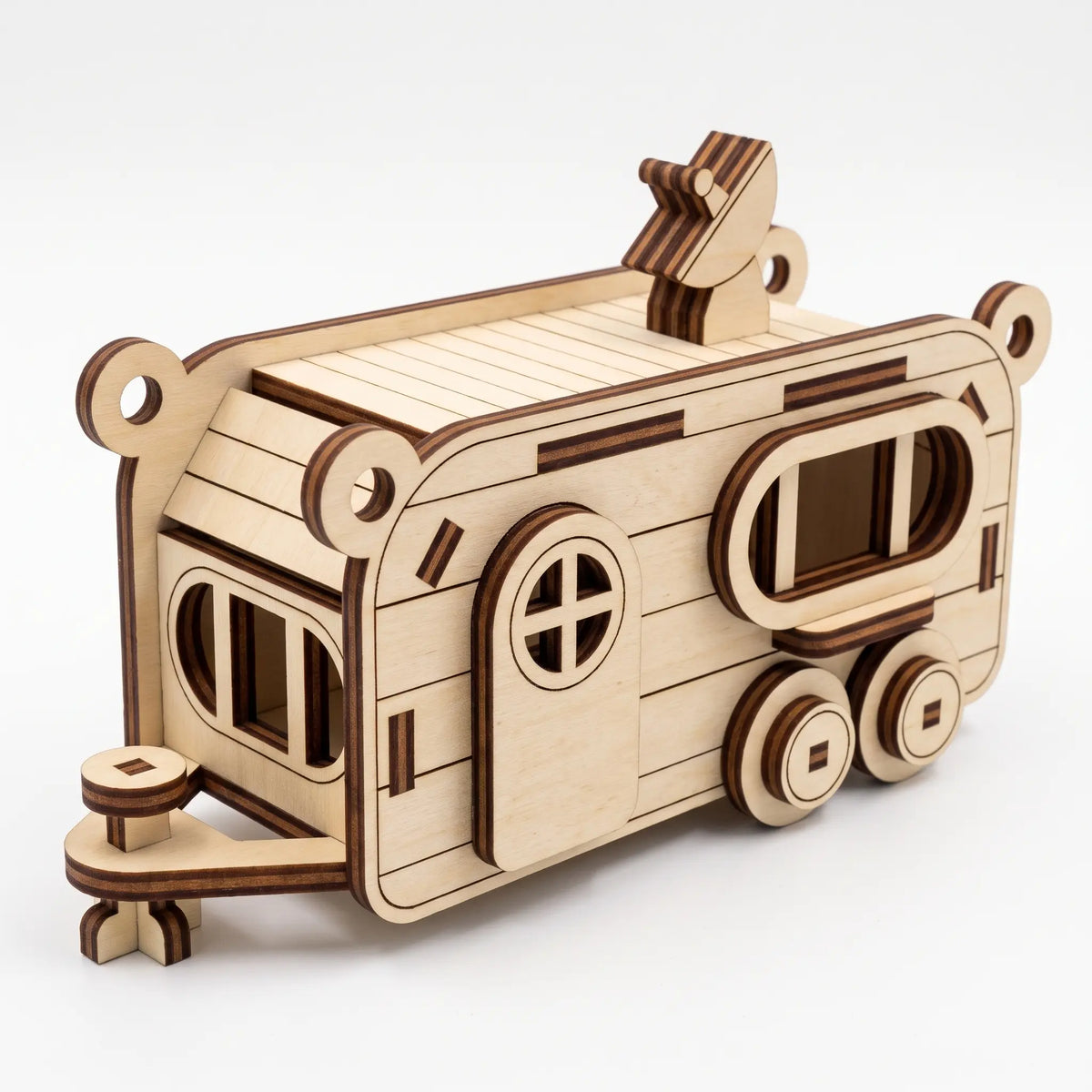 3D laser cut plywood camper trailer model with hitch coupler, rounded door, and roof antenna on plain white backdrop.