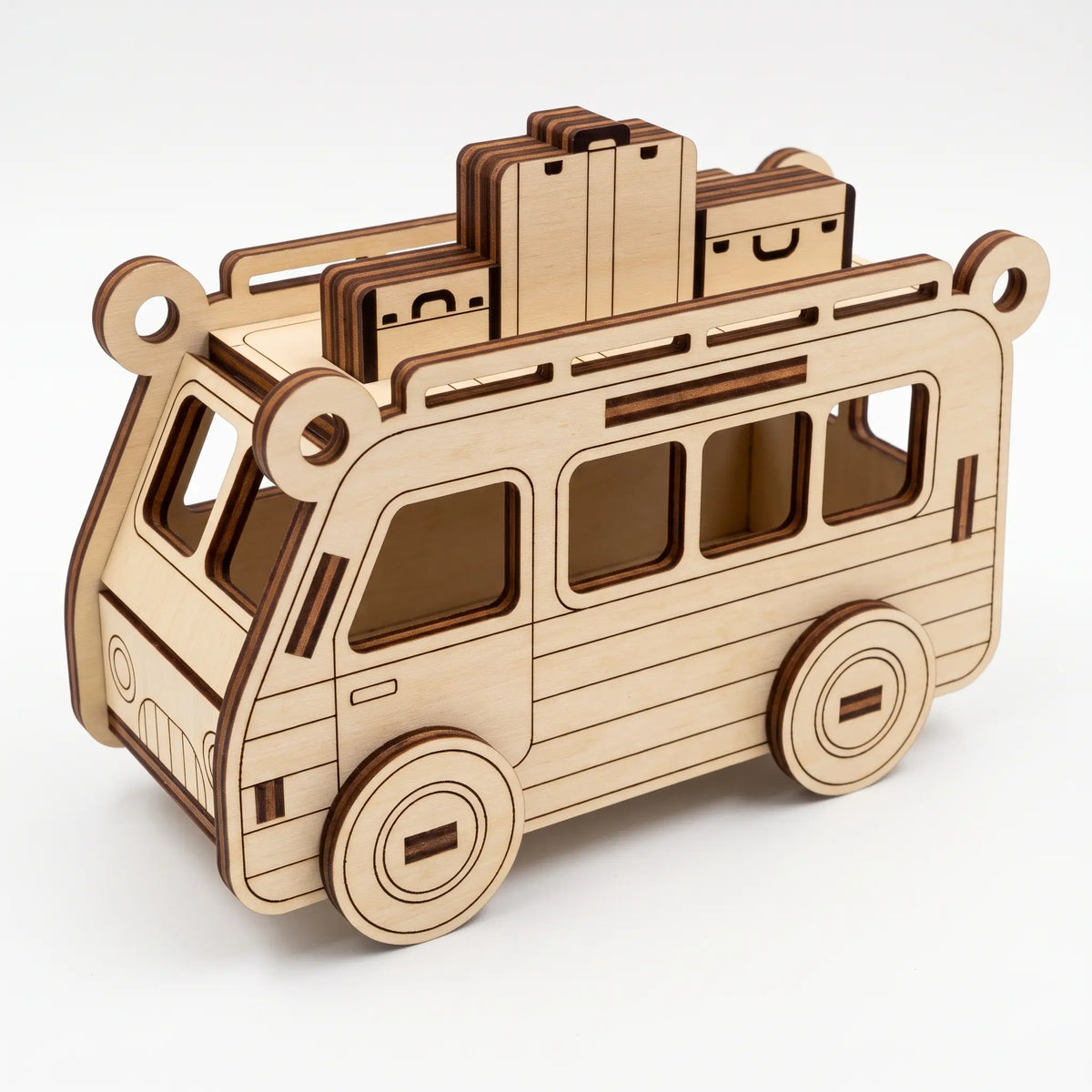 Natural laser cut plywood travel bus model carrying layered suitcases on top roof rack against plain white backdrop.