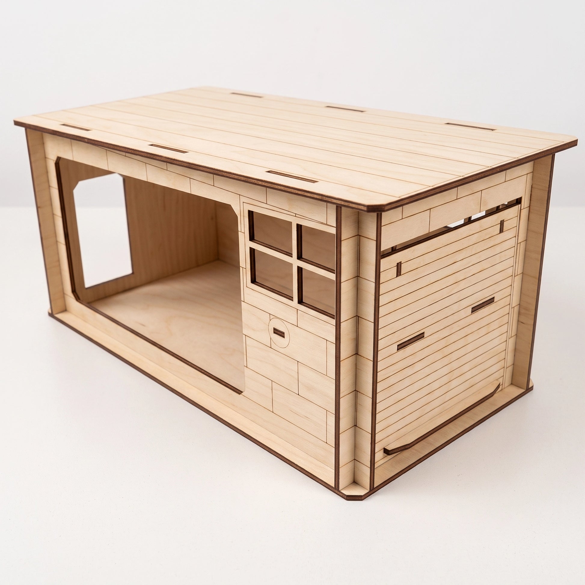 Three-quarter studio view of the unassembled laser-cut plywood garage kit on a white surface
