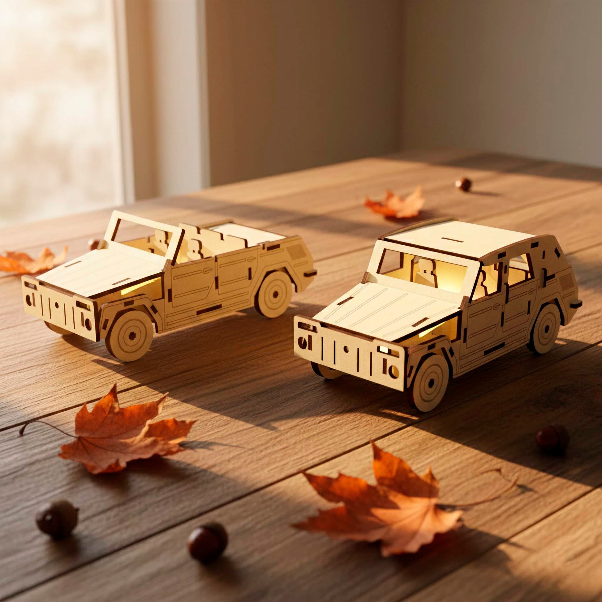 Two laser cut wooden car models shown together on a sunlit wooden table. One model features an open-top convertible design, while the other has a full roof. Both 3D puzzles are surrounded by scattered autumn leaves and acorns