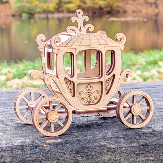 Wooden miniature carriage displayed outdoors on a rustic wooden surface, surrounded by autumn forest colors, showcasing laser-cut details and elegant wheel design.