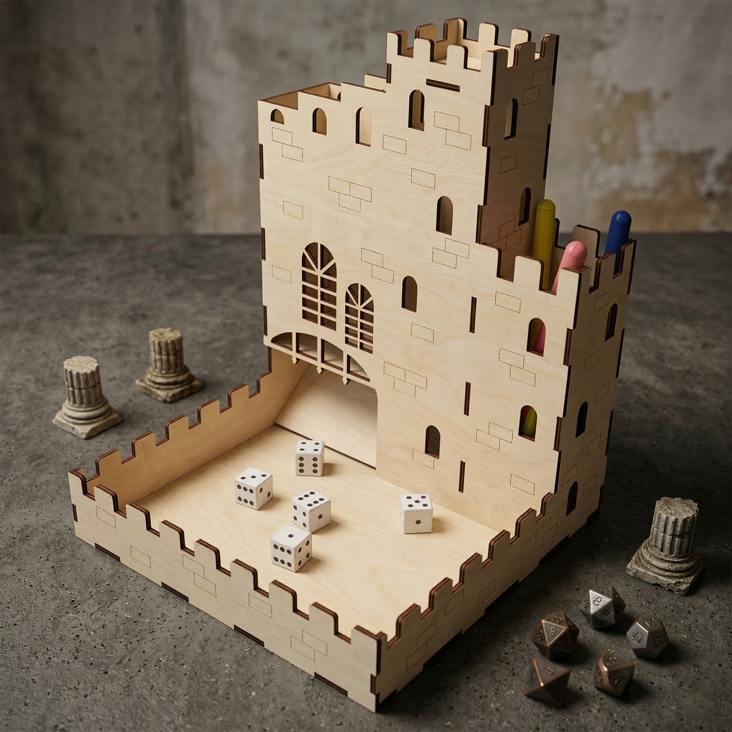 Castle dice tower made of laser cut plywood with etched stone patterns and arched windows. White dice rest in the crenelated tray. Features a built-in pen holder on the side. Shown on a grey stone surface with miniature ruins.
