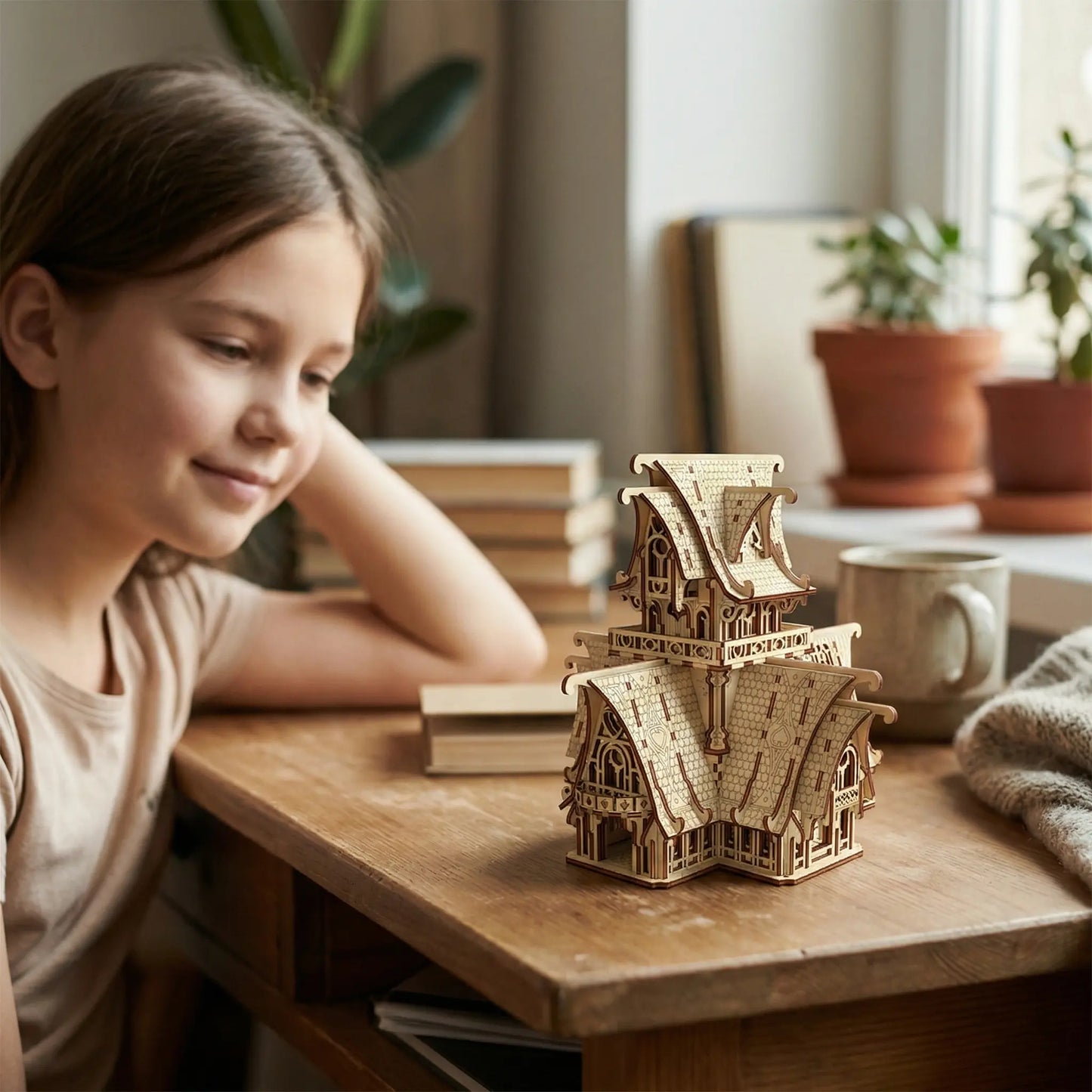 Young girl sitting at a wooden table with a wooden laser cut model house and books.