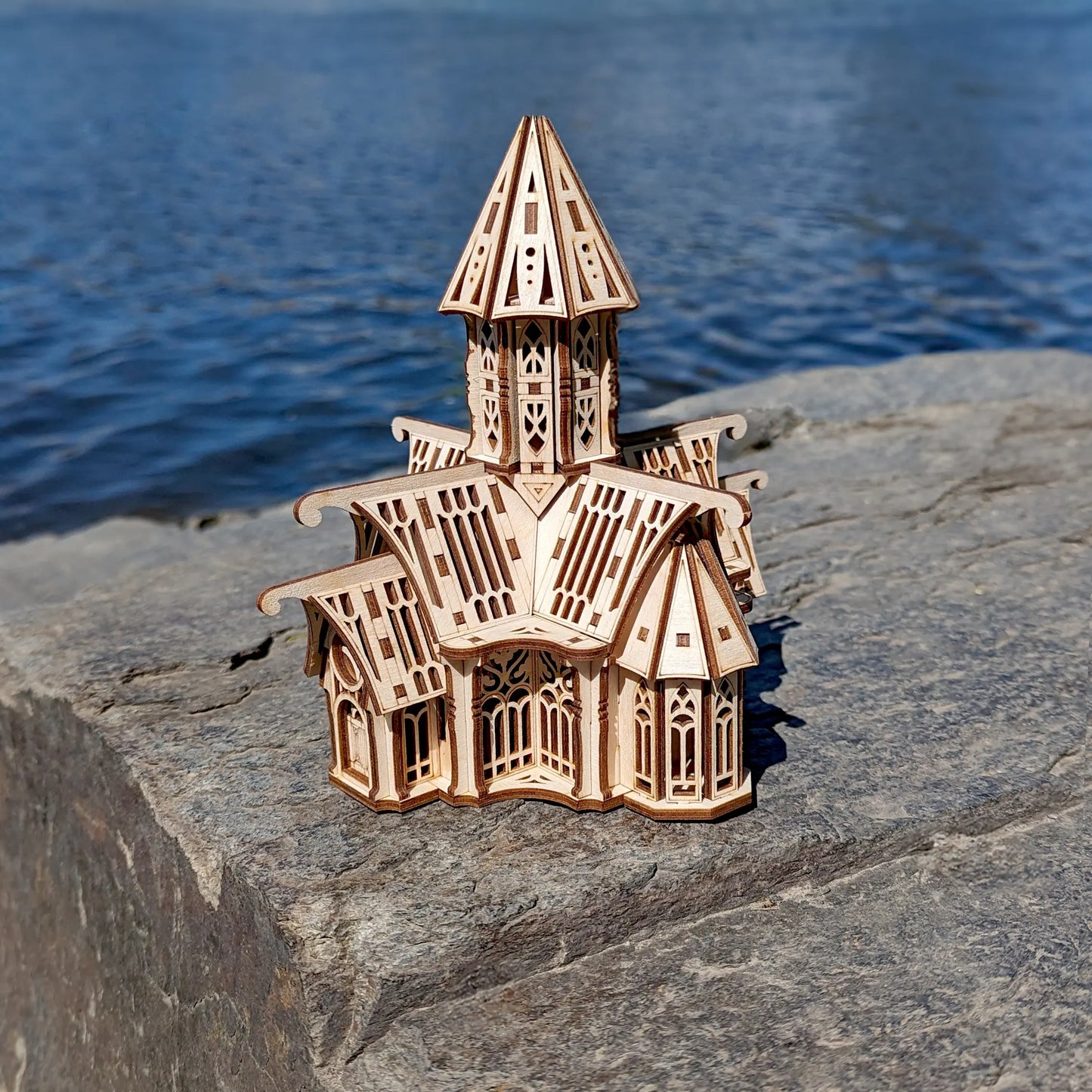 High-angle shot of an architectural laser cut plywood cathedral model sitting on a stone block near a river shore.