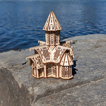 High-angle shot of an architectural laser cut plywood cathedral model sitting on a stone block near a river shore.